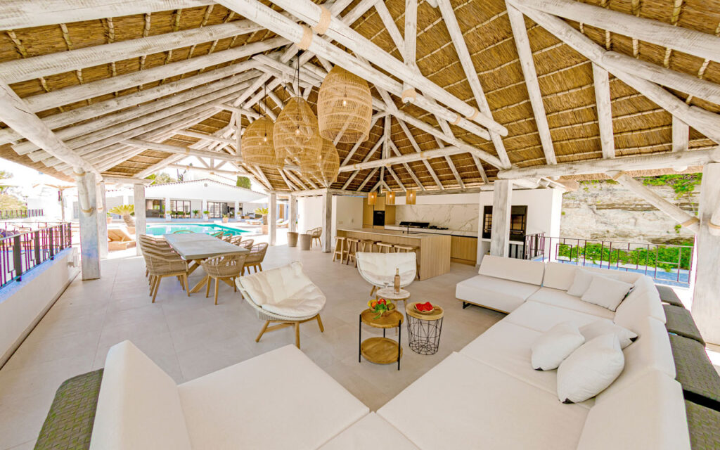 Thatched roof with white-washed beams over an open-plan outdoor living and kitchen area beside a pool