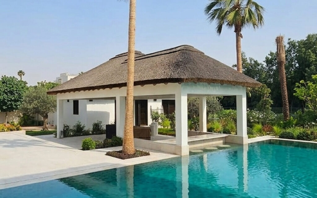 Open-sided thatched entertainment pavilion with swim-up pool bar and modern outdoor seating, Al Barari Dubai residential project by Cape Reed
