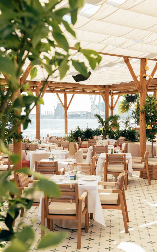 Restaurant dining tables set beneath Cape Reed's natural timber pergola structure at Giulia by the Beach, Dubai, with lemon trees framing the open waterfront view